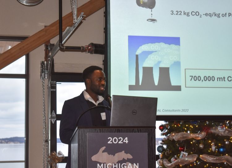 MSU PhD Student, Manasseh Agbedam, standing at a podium with a big screen behind him.