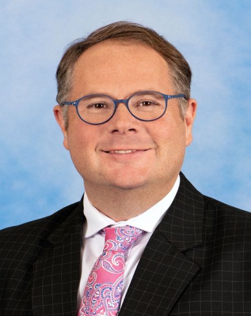 A headshot of Joseph Hune wearing a suit and pink-patterned tie.