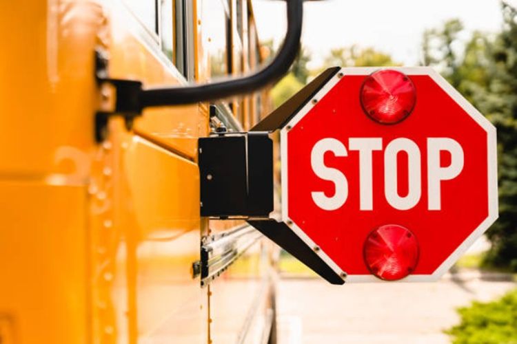 The side of a yellow school bus with a red stop sign stuck out from the side.
