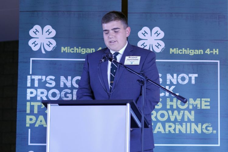 A young man in a suit in front of two banners.