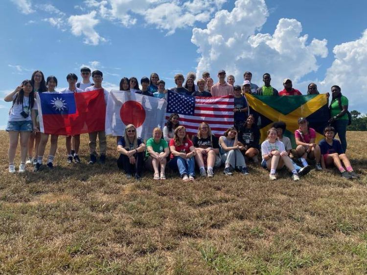 A group of diverse people outside in front of a blue sky, holding up various flags.