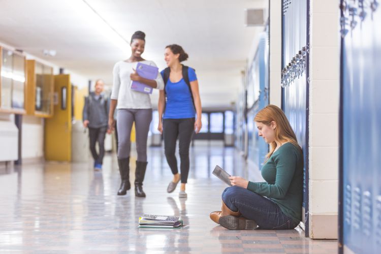 Two smiling youth walking down a school hallway with another student sitting against a locker.
