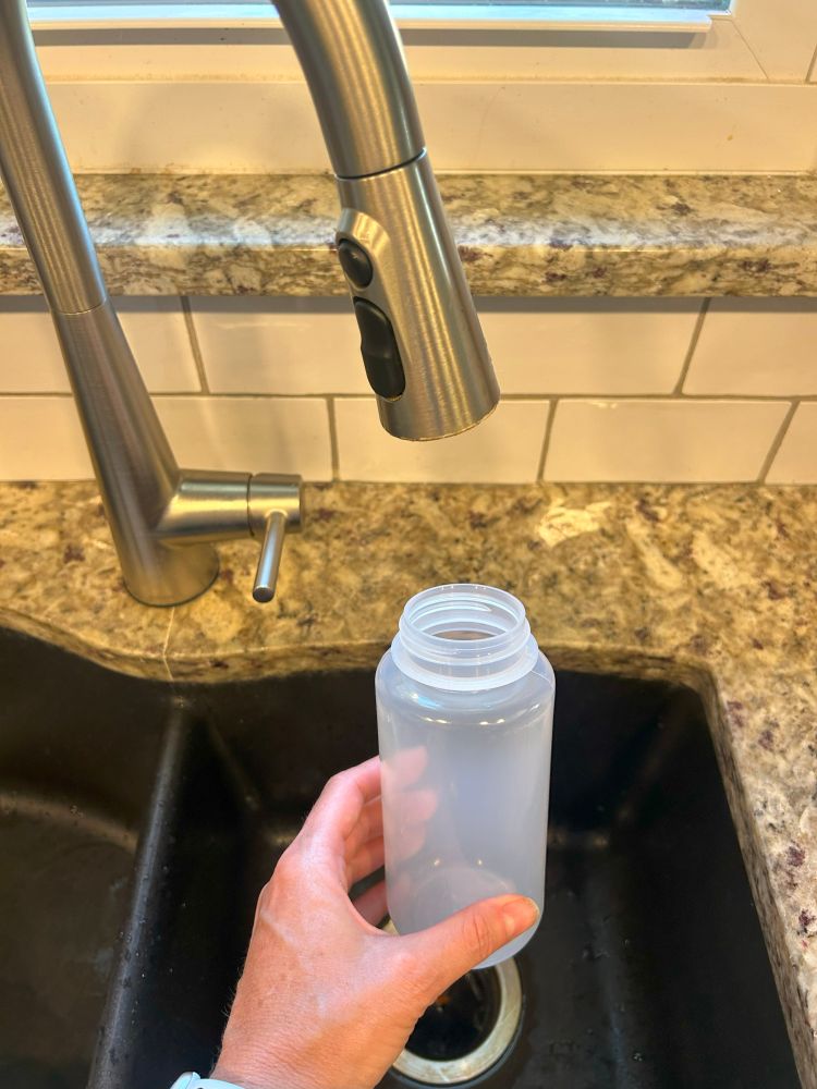 A sample bottle at a kitchen faucet for PFAS sampling.