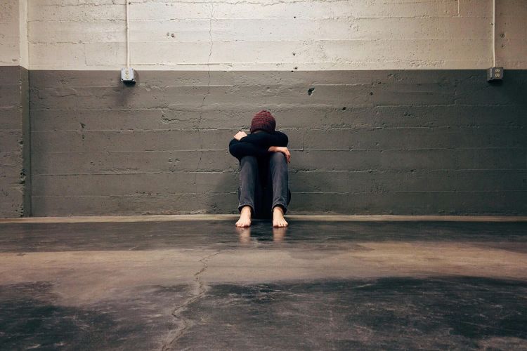 Someone sitting against a wall with their head on their knees.