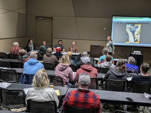 A conference room with a panel of four farmers, a moderator and about 20 audience members.