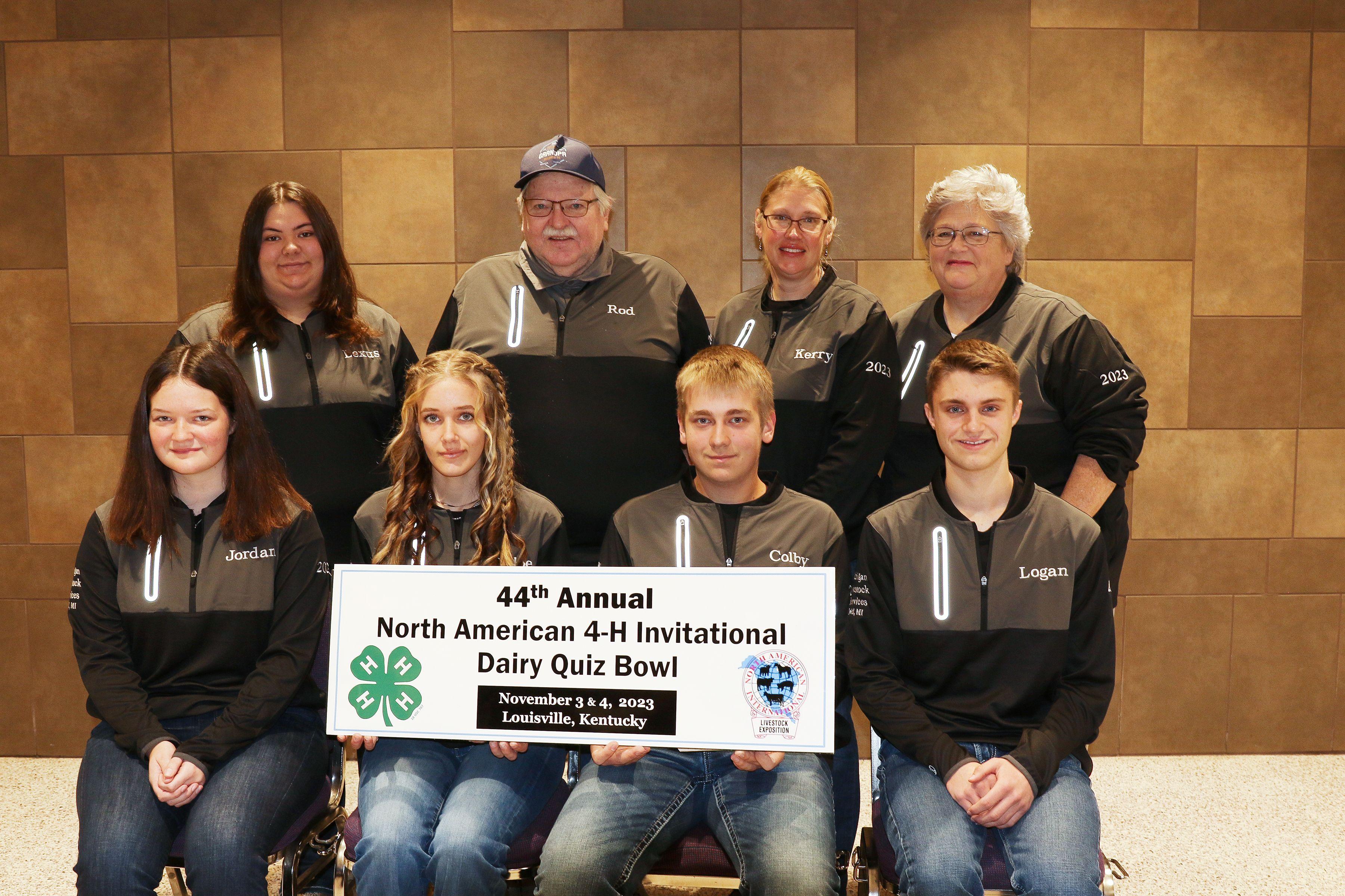 Team members sitting infront of a sign.