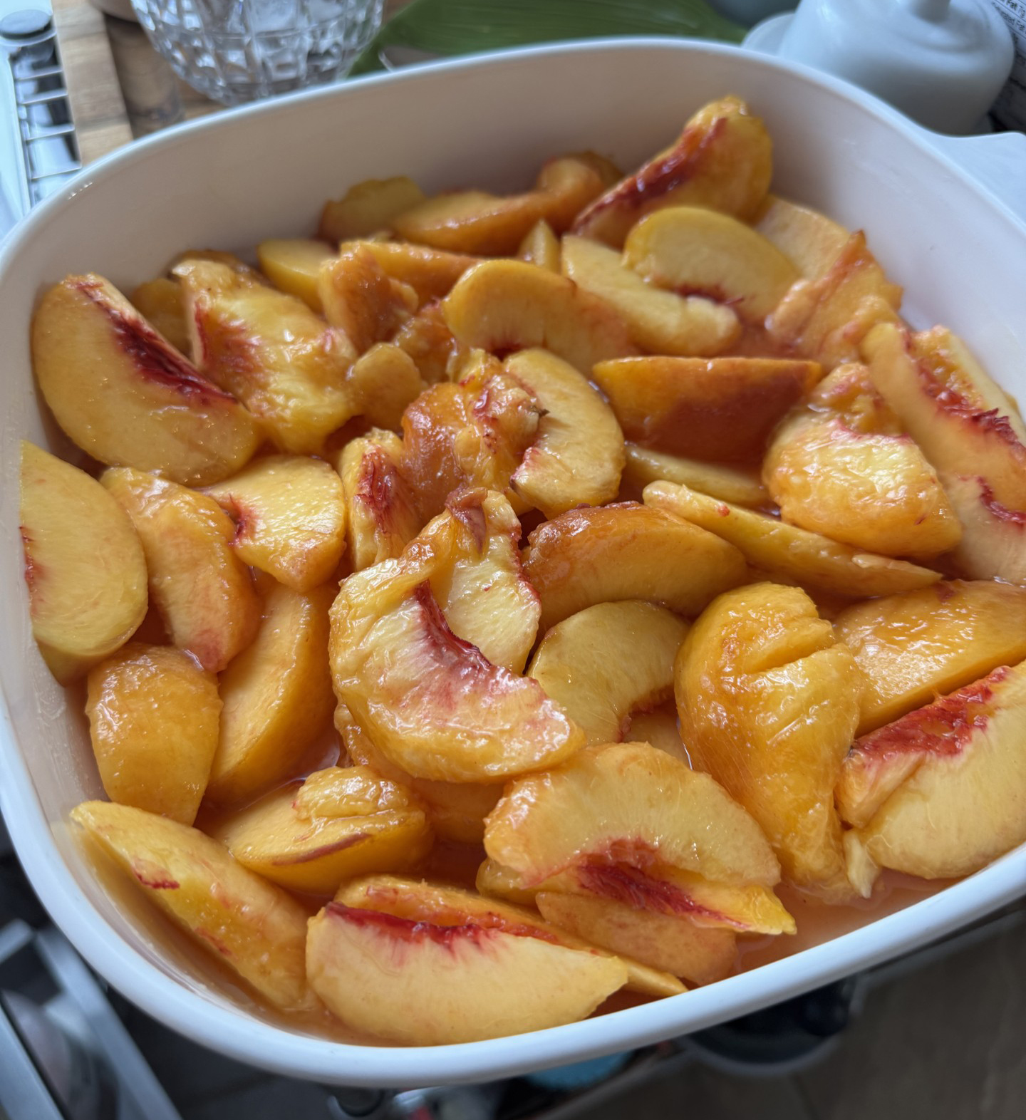 A white baking dish filled with freshly sliced Red Haven peaches, golden-orange with streaks of red near the skins.