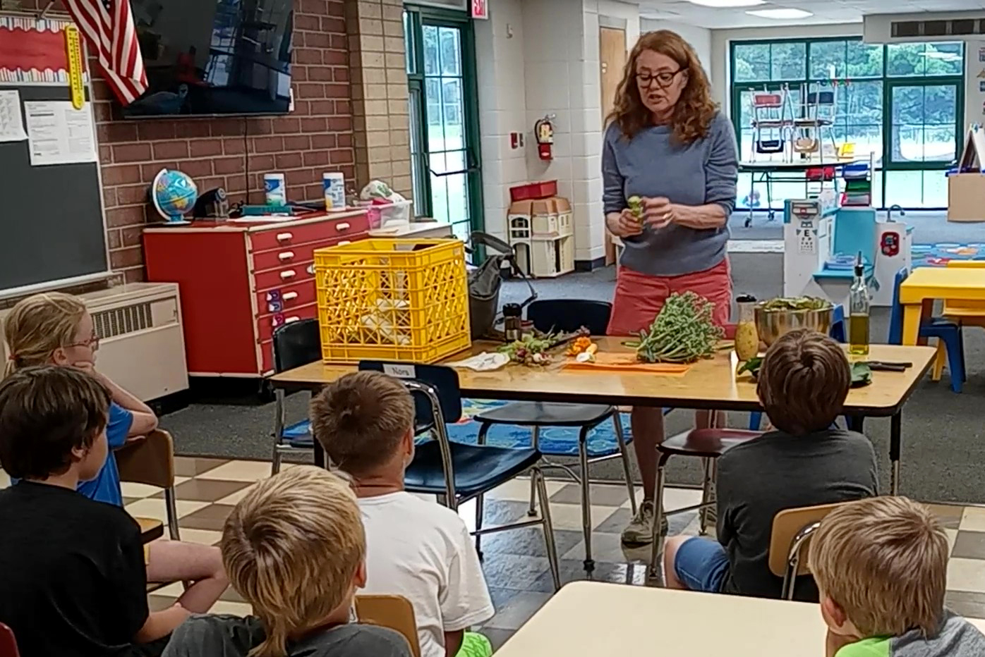 A woman stands in front of a classroom holding vegetables.